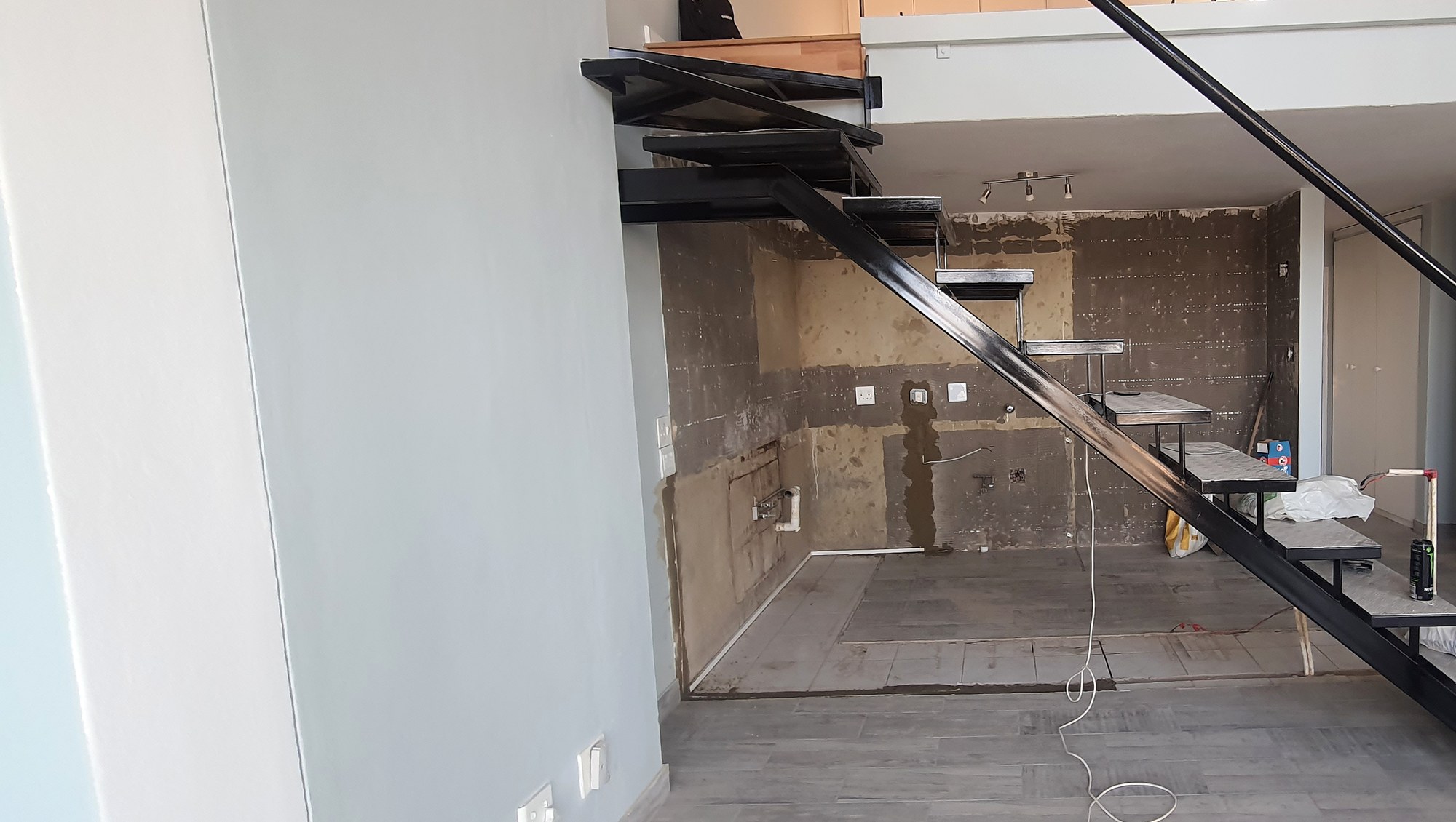 Strip-out. Tiles off the kitchen wall, black stair still in place.
